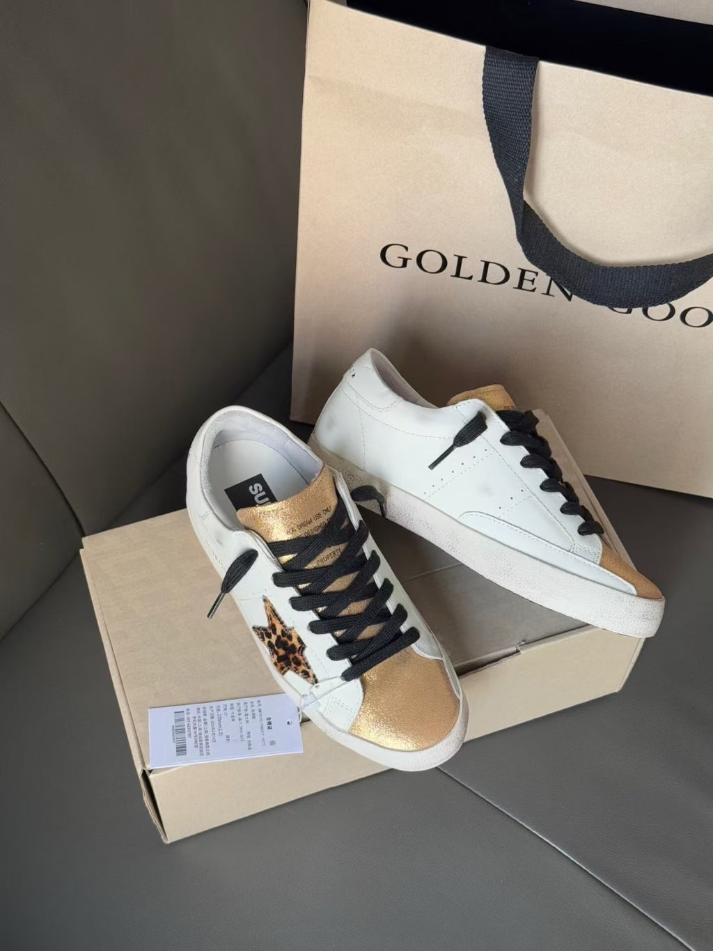 White low-top sneakers with black laces, gold trim, and leopard print side accent