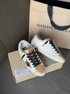 White leather sneakers with black laces, leopard star detail, and gold metallic toe sections.