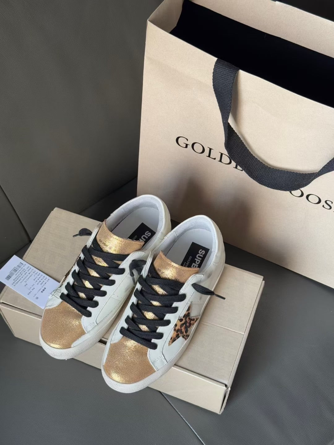 Pair of white low-top sneakers with black laces, gold accents, and leopard print detail