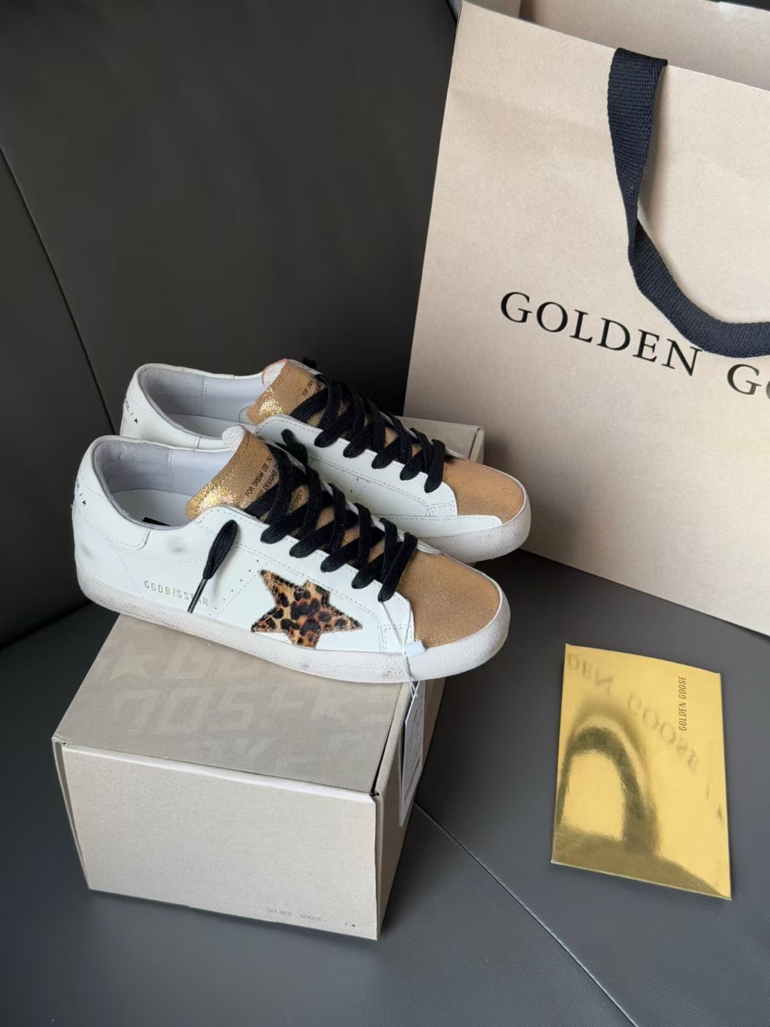 White low-top sneakers with black laces, gold accents, and leopard print panel