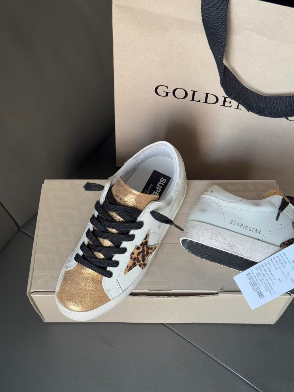 White leather sneaker with black laces, leopard star patch, and gold toe cap.