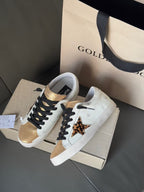 White low-top sneakers on shoebox, black laces, gold accents, and leopard print panels