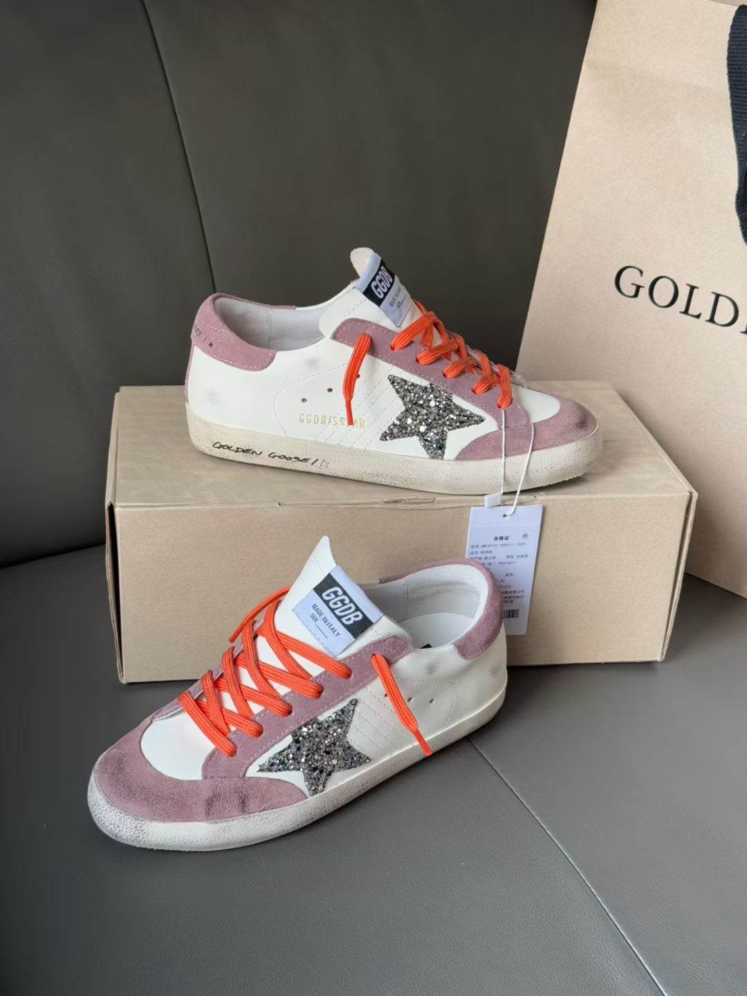 Pair of high-top sneakers on shoebox, orange laces, white and lilac uppers, glitter star
