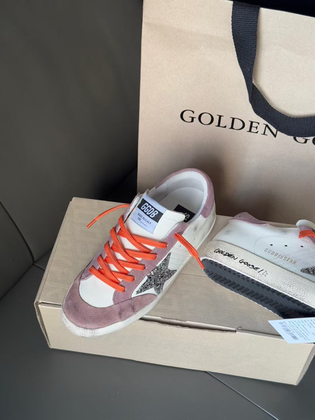 High-top sneakers on shoebox, orange laces, white and lilac panels, glitter side star
