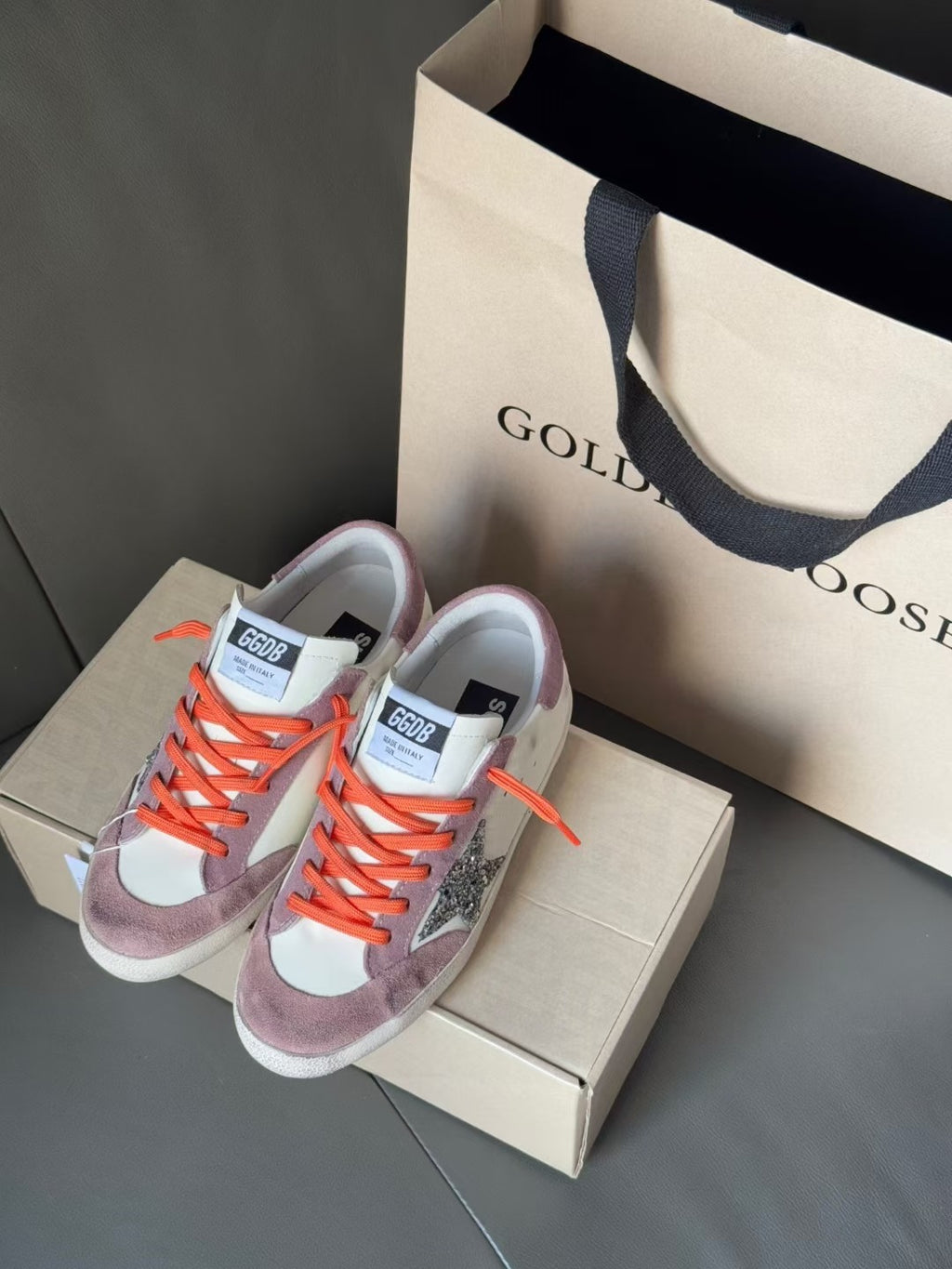 Pair of high-top sneakers on shoebox, orange laces, white and lilac uppers, side glitter star