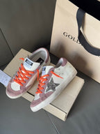 High-top sneakers on shoebox, orange laces, white and lilac panels, glitter star on side
