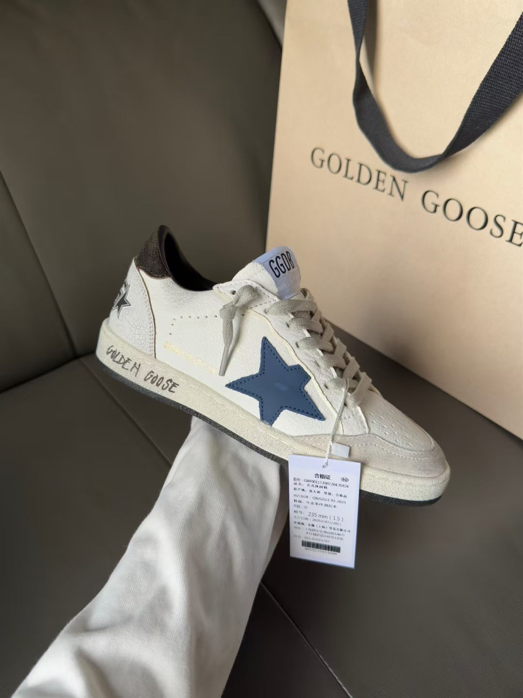White low-top sneakers with blue star patch, black collar, lace-up front on box