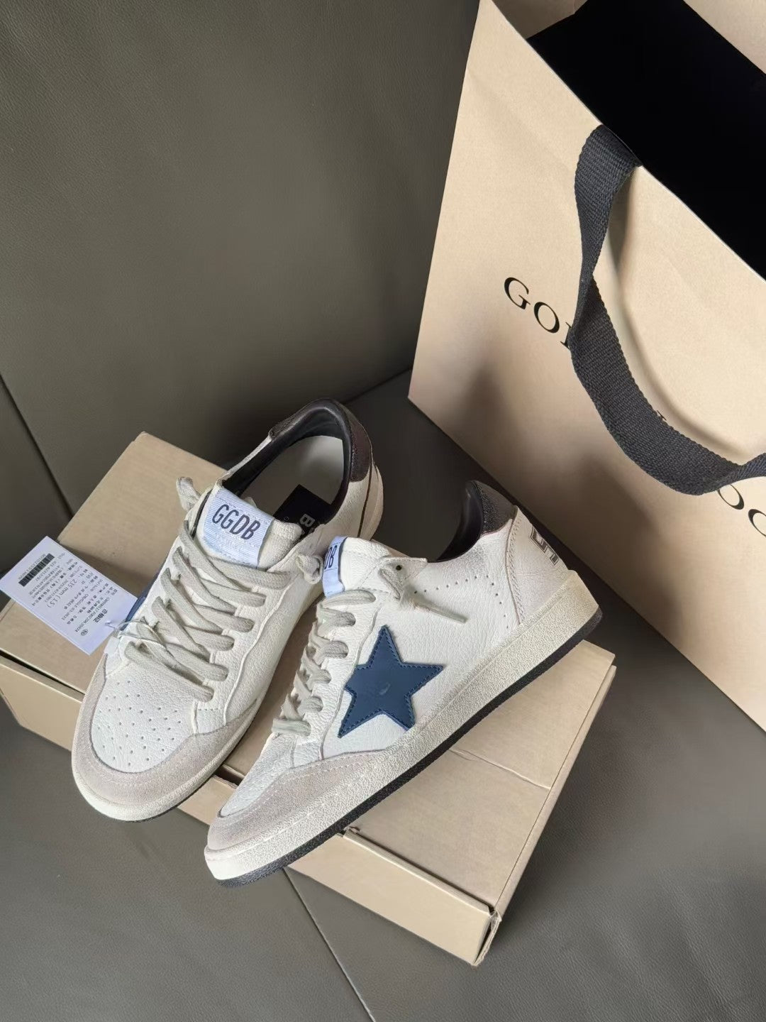 White sneakers with blue star emblem and black heel, shown at side angle with tags