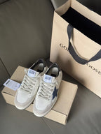White sneakers with blue star logo and black heel accents, front view on shoe boxes