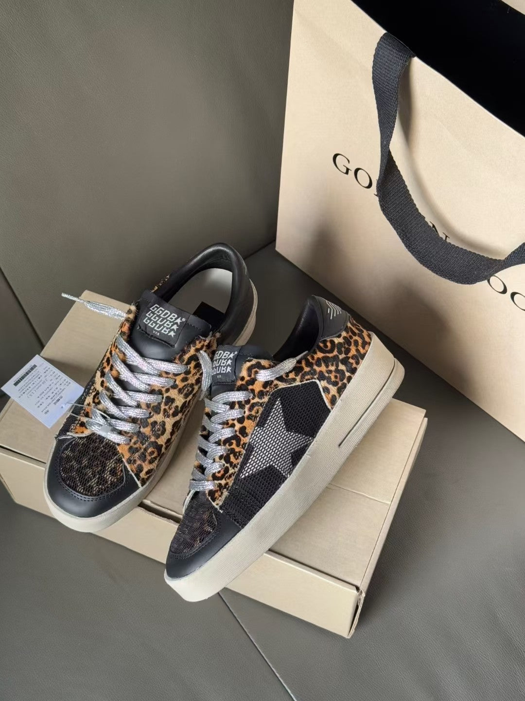 Low-top leopard-print lace-up sneakers with dark uppers and white rubber soles on boxes