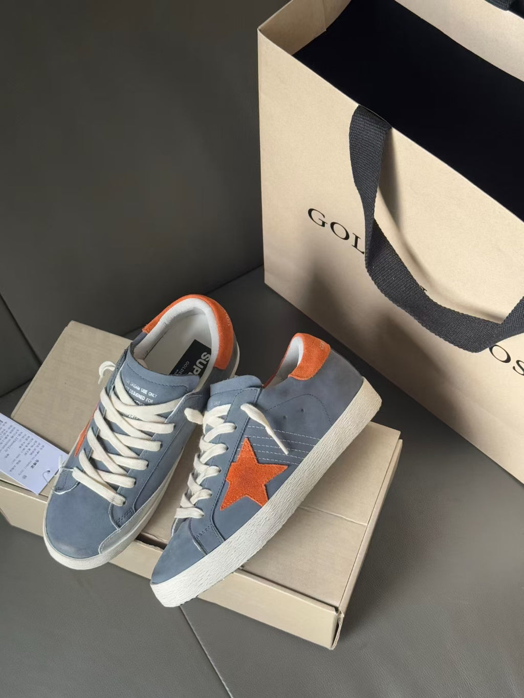Golden Goose light blue sneakers with orange star patch, shown front and angled