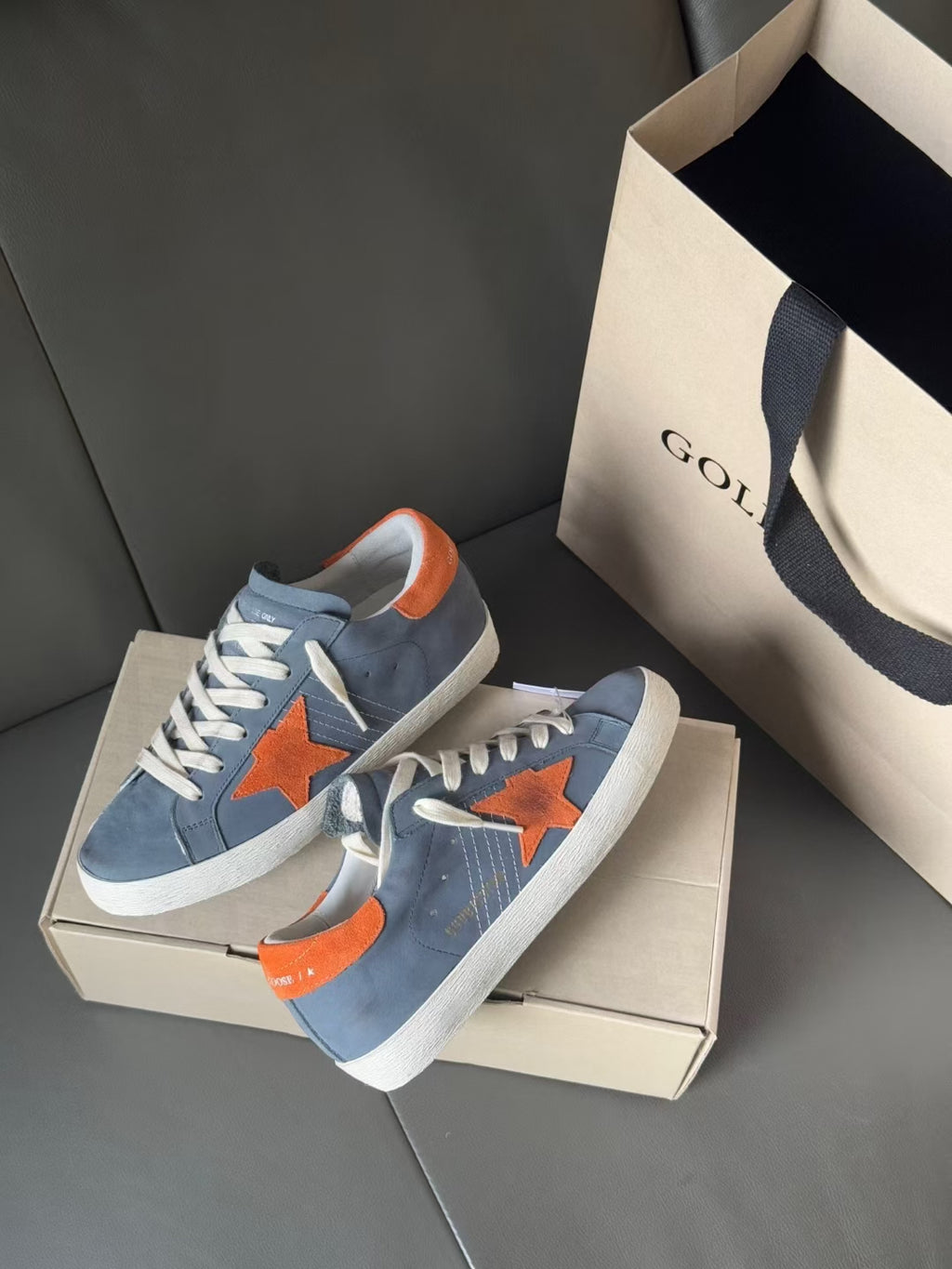 Pair of light blue low-top Golden Goose sneakers with orange star applique and white sole
