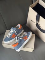 Golden Goose low-top sneakers in blue with orange star accents and white rubber sole.