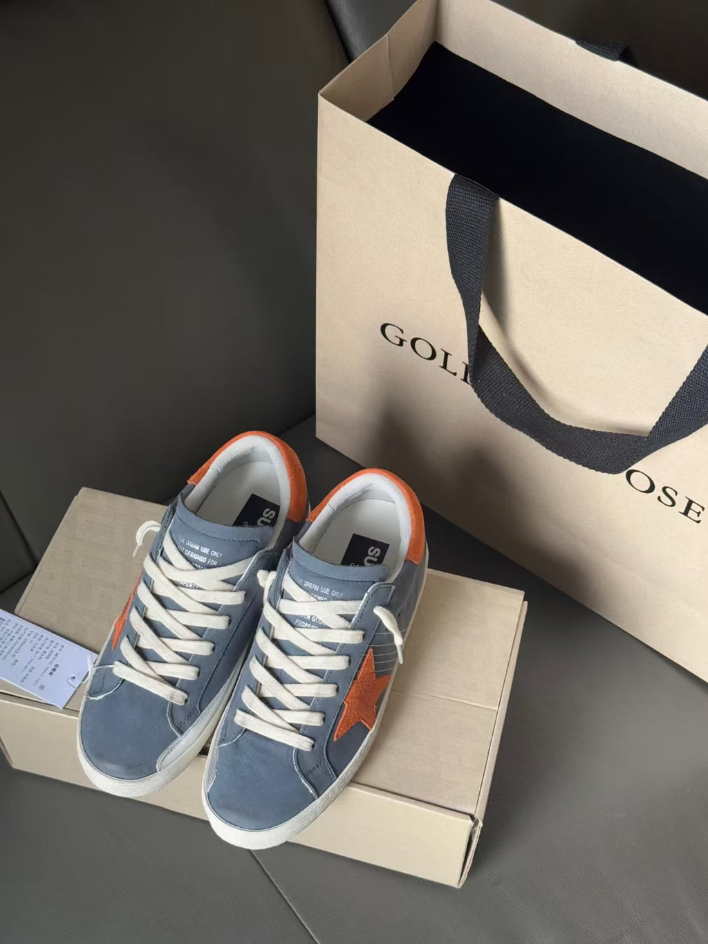 Light blue Golden Goose sneakers on shoebox, orange star patch and orange heel lining
