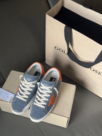 Golden Goose low-top sneakers in blue with orange star patch, white laces and sole.