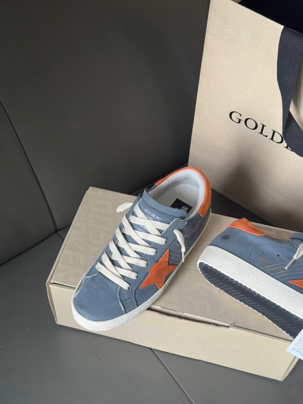 Golden Goose blue low-top sneakers with orange star patch, orange heel tab, white sole.