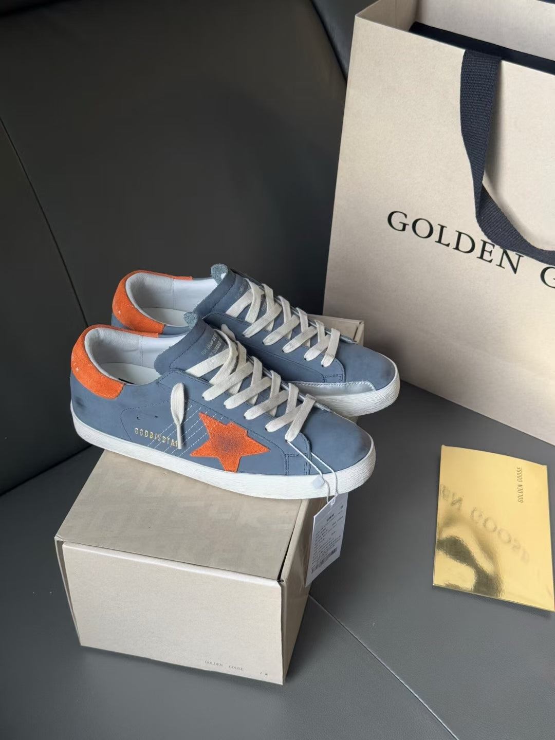 Golden Goose sneakers in blue with orange star motif, white laces, and orange heel trim.