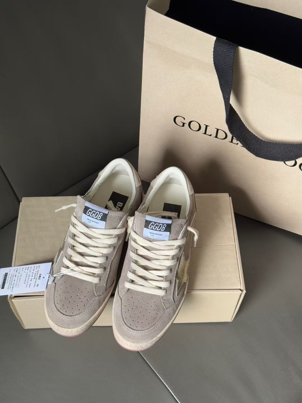 Light gray low-top sneakers, white laces, metallic star overlays, pink outsole edge