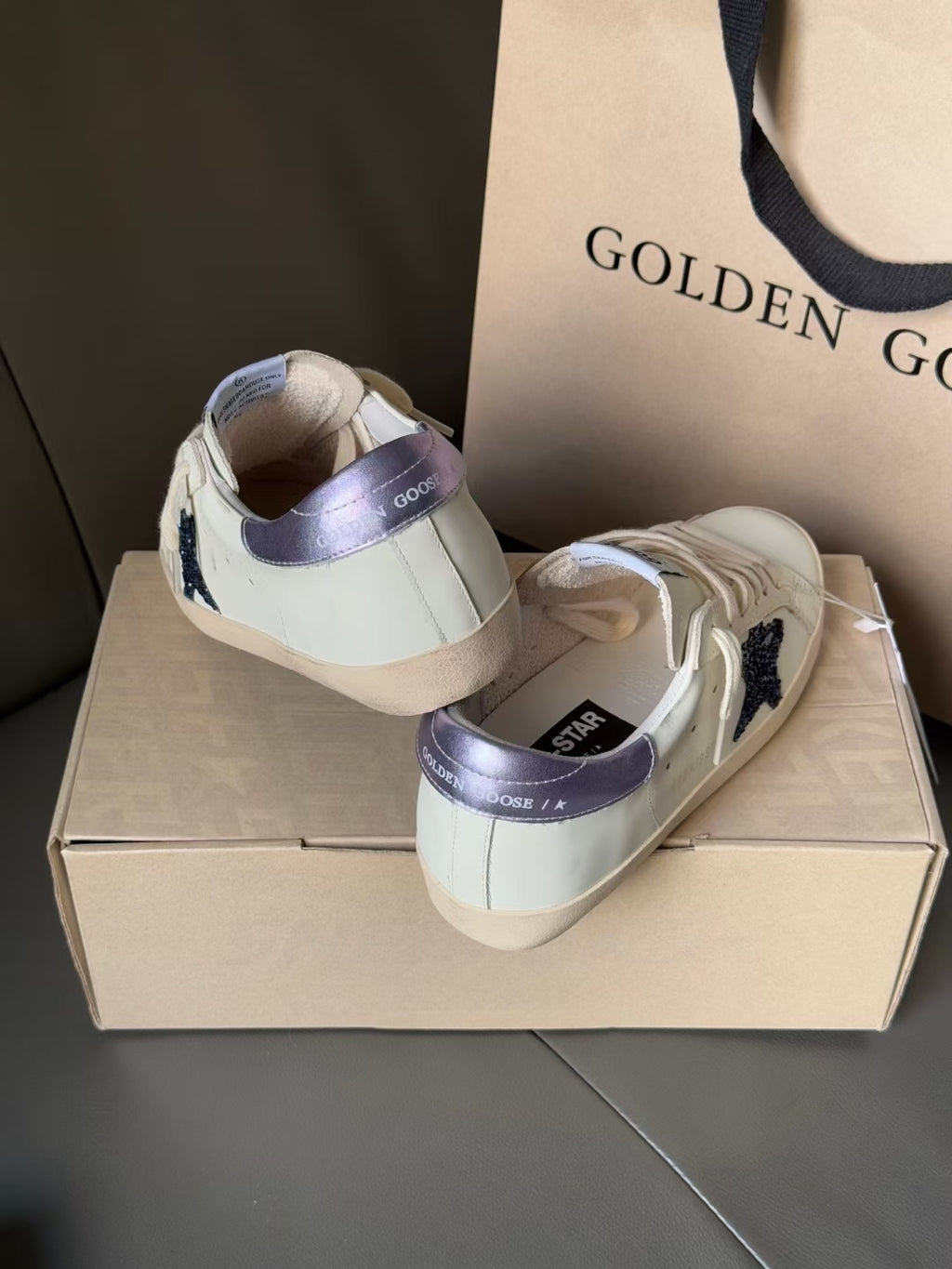White luxury sneakers with navy star detail and lavender lining, on box