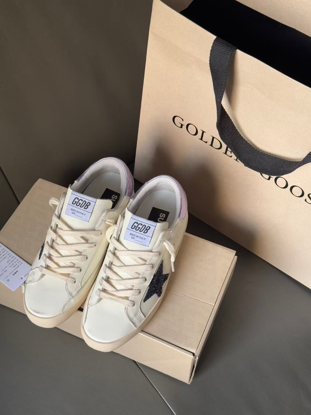 White luxury sneakers with navy star and lace-up closure, shown on box