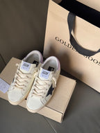 White luxury sneakers with navy star and lace-up closure, shown on box