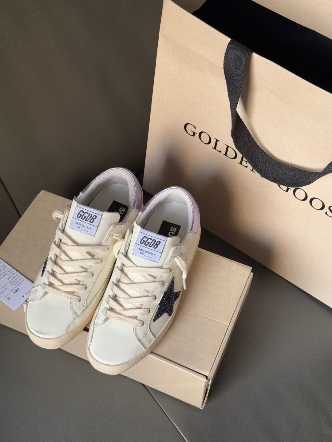 White luxury sneakers with navy star and lace-up closure, shown on box