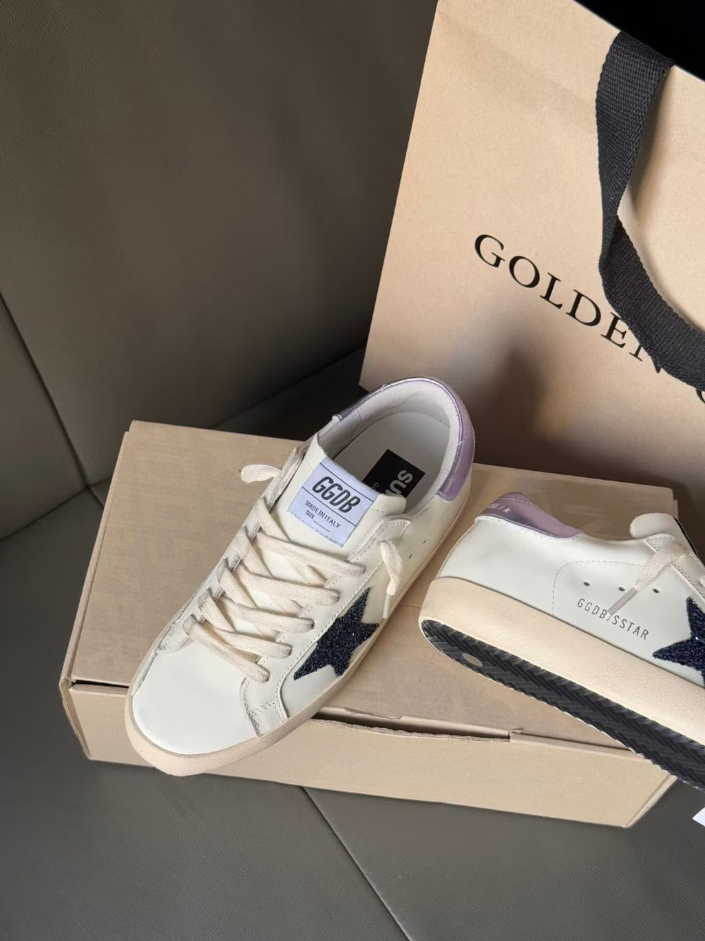 Side-by-side luxury sneakers, white with navy star and lavender heel accents, on boxes