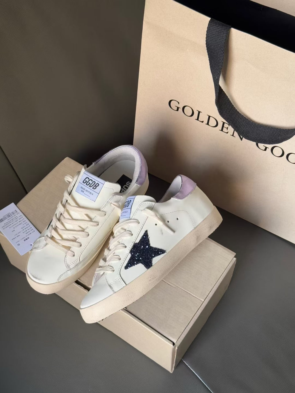 White luxury sneakers with navy star and lavender heel lining, on shoebox