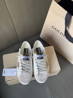 White lace-up sneakers with gold glitter star patch, shown with box and tags