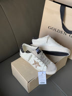 White low-top sneakers with gold glitter star patch and dark heel trim