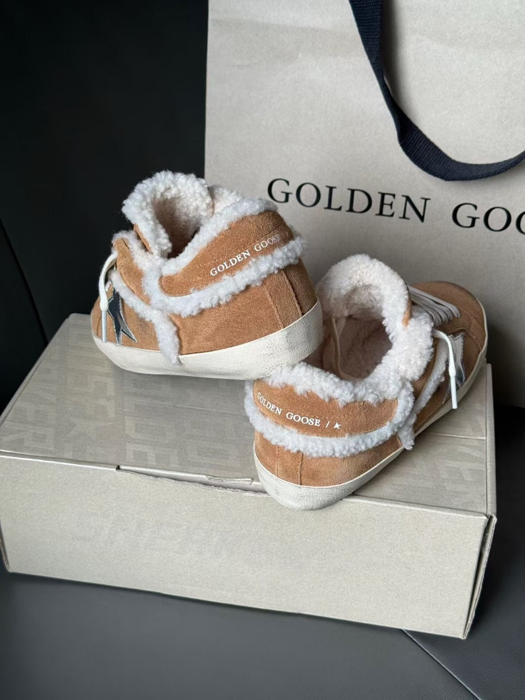 Pair of brown suede high-top sneakers with white shearling lining, blue star logo, white laces.
