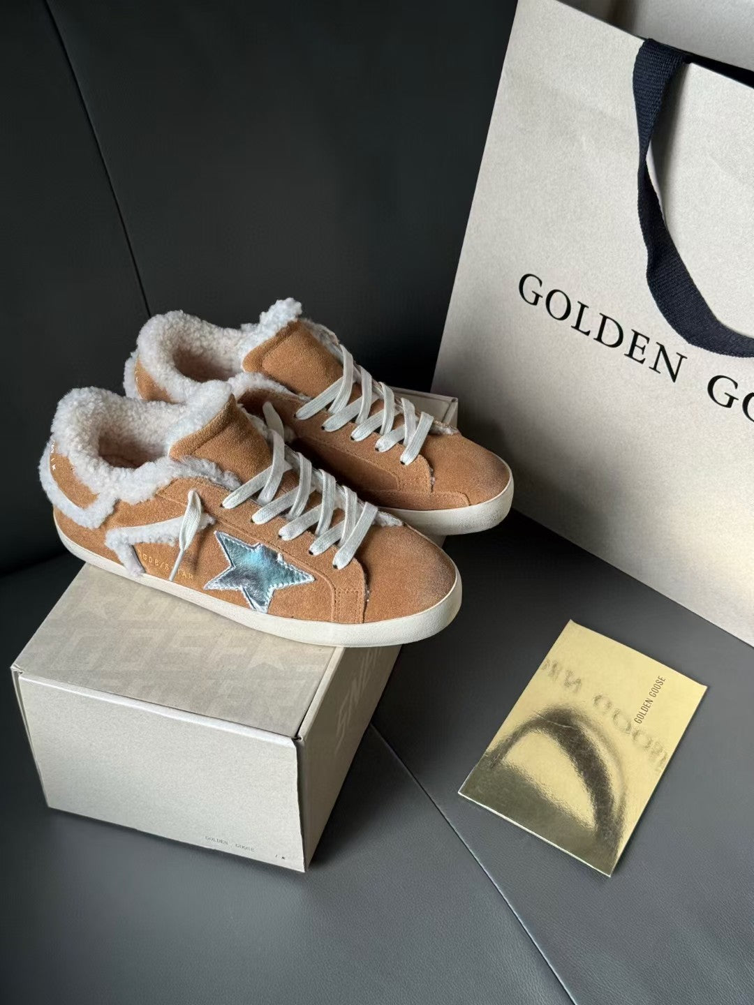 Brown suede high-top sneakers with white shearling trim and blue star patch, on a box.