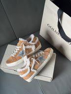 Brown suede sneakers with white shearling trim and blue star patches, shown on a box.