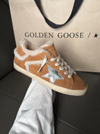 Brown suede high-top sneakers with white shearling trim, blue star patch, and white laces.