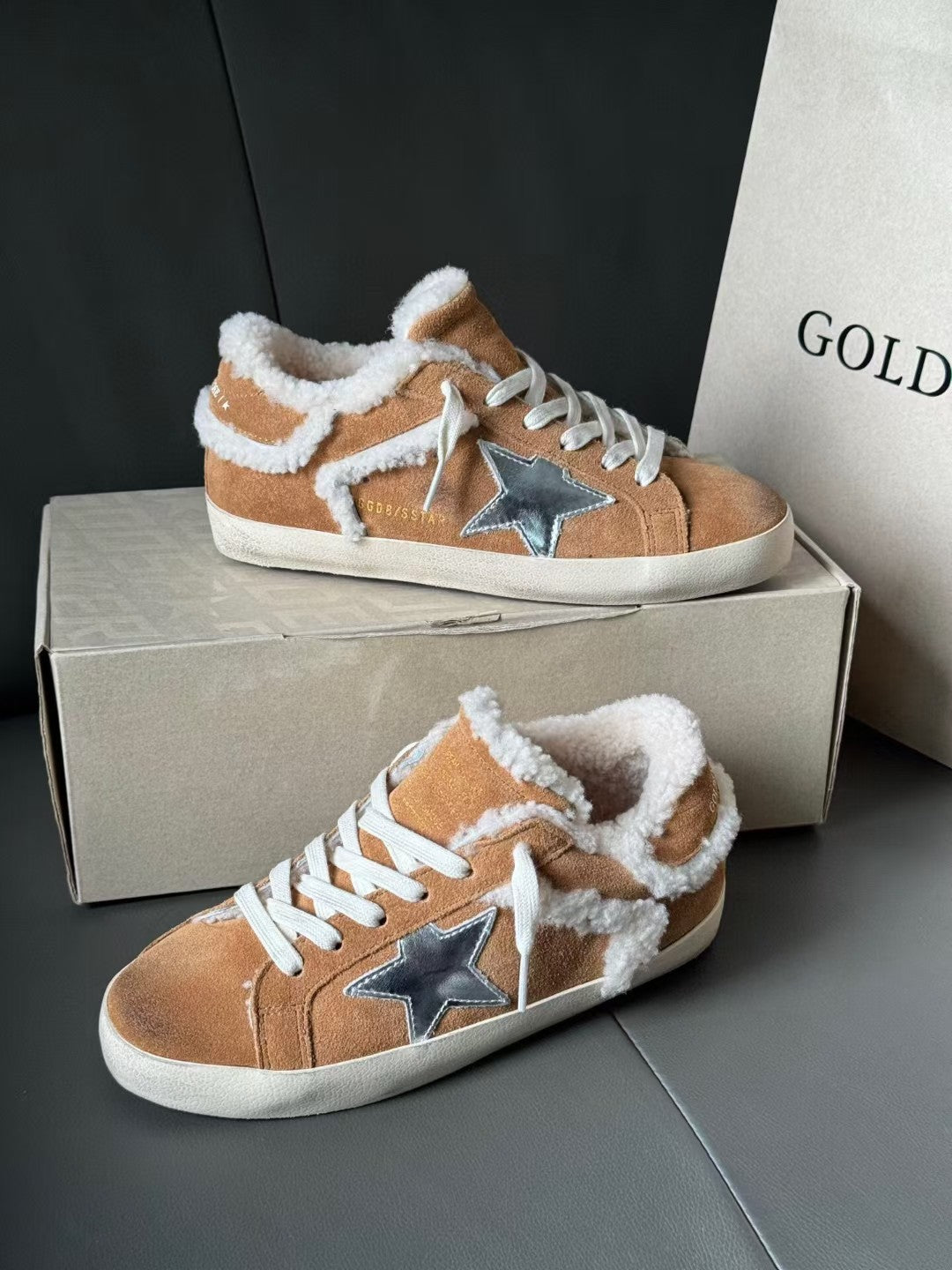 Brown suede high-top sneakers with white shearling trim, blue star patches, and white laces.