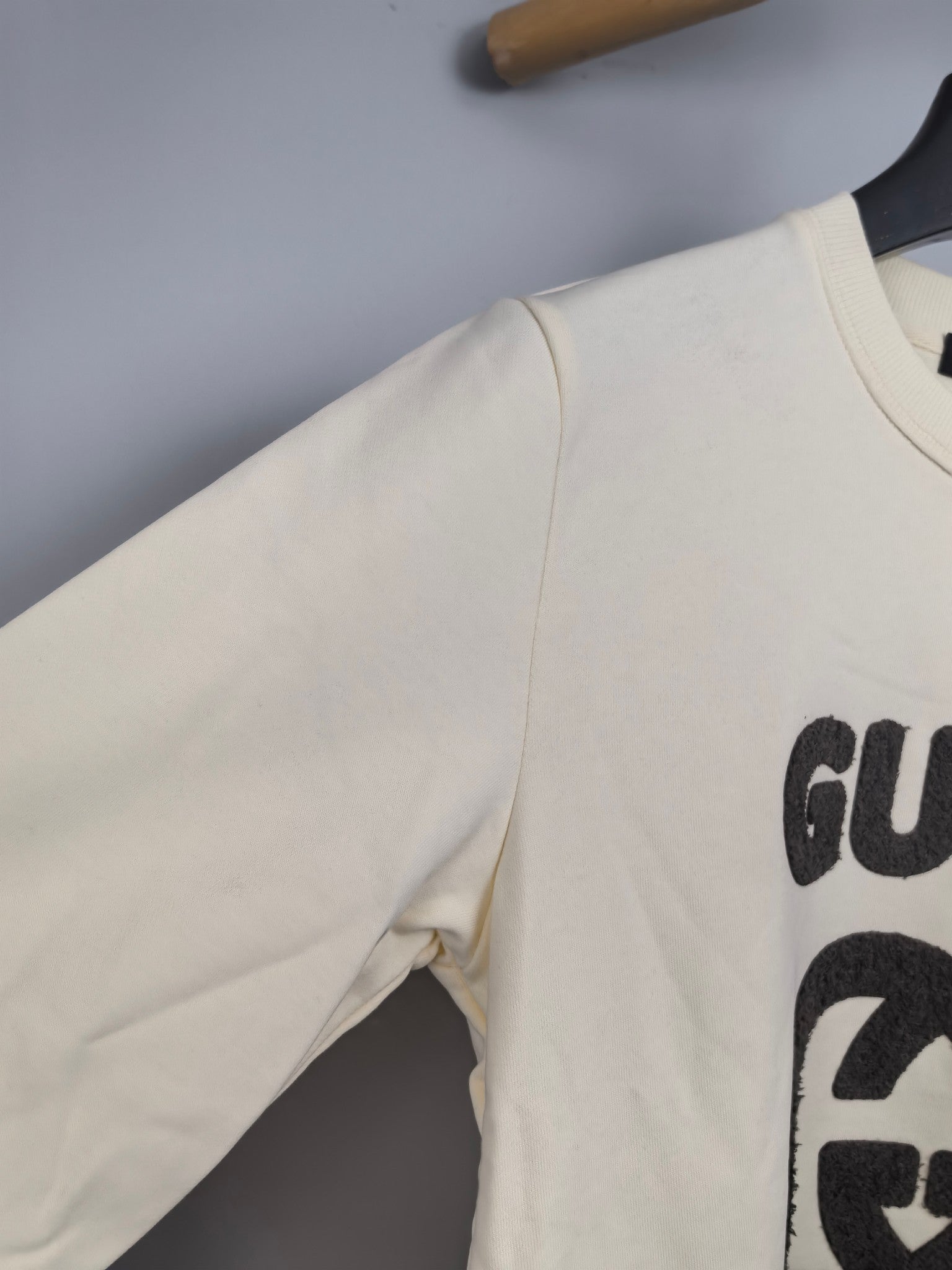 Cream sweatshirt sleeve detail with partial black GUCCI logo