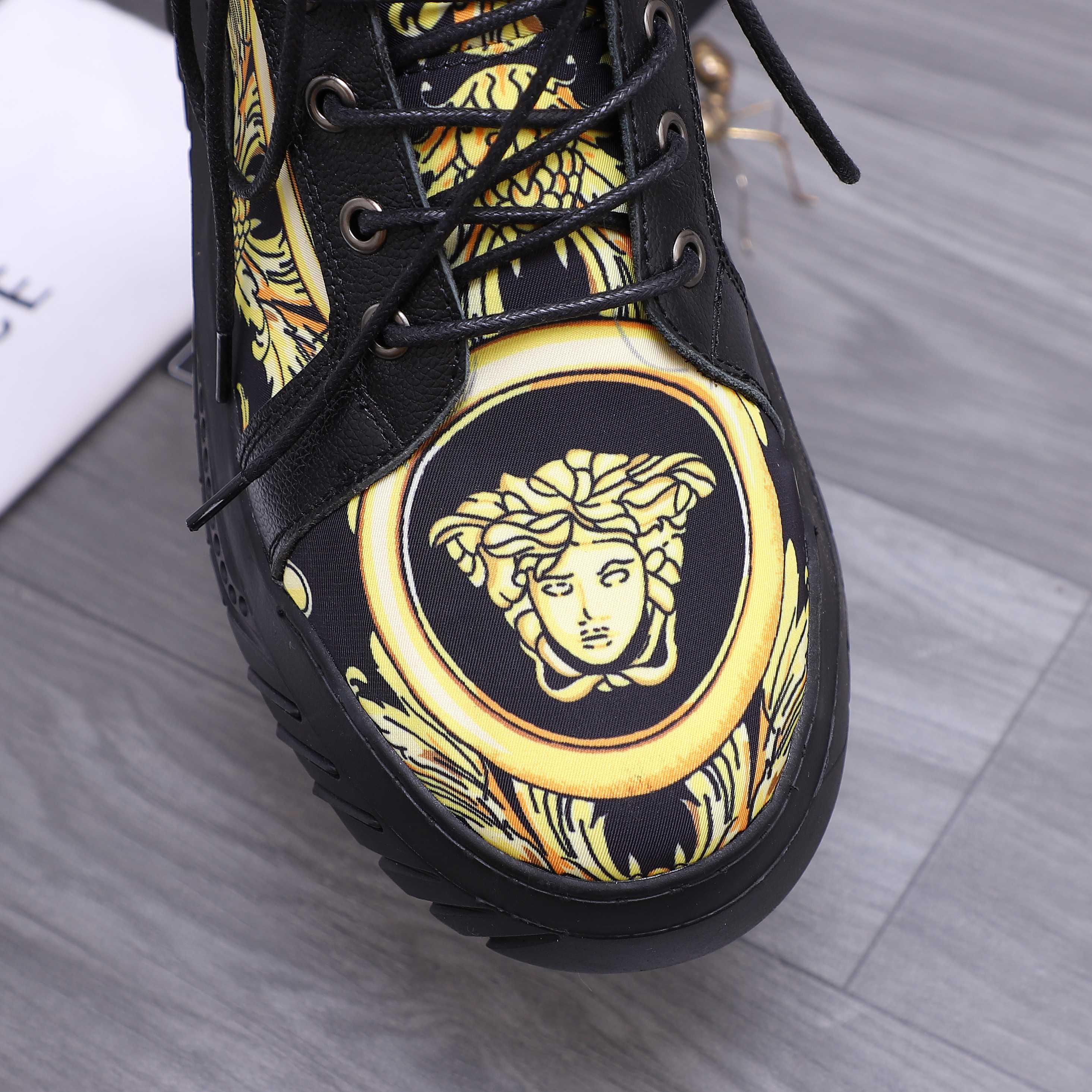 Close-up of black high-top sneaker toe with gold Medusa emblem and lace eyelets