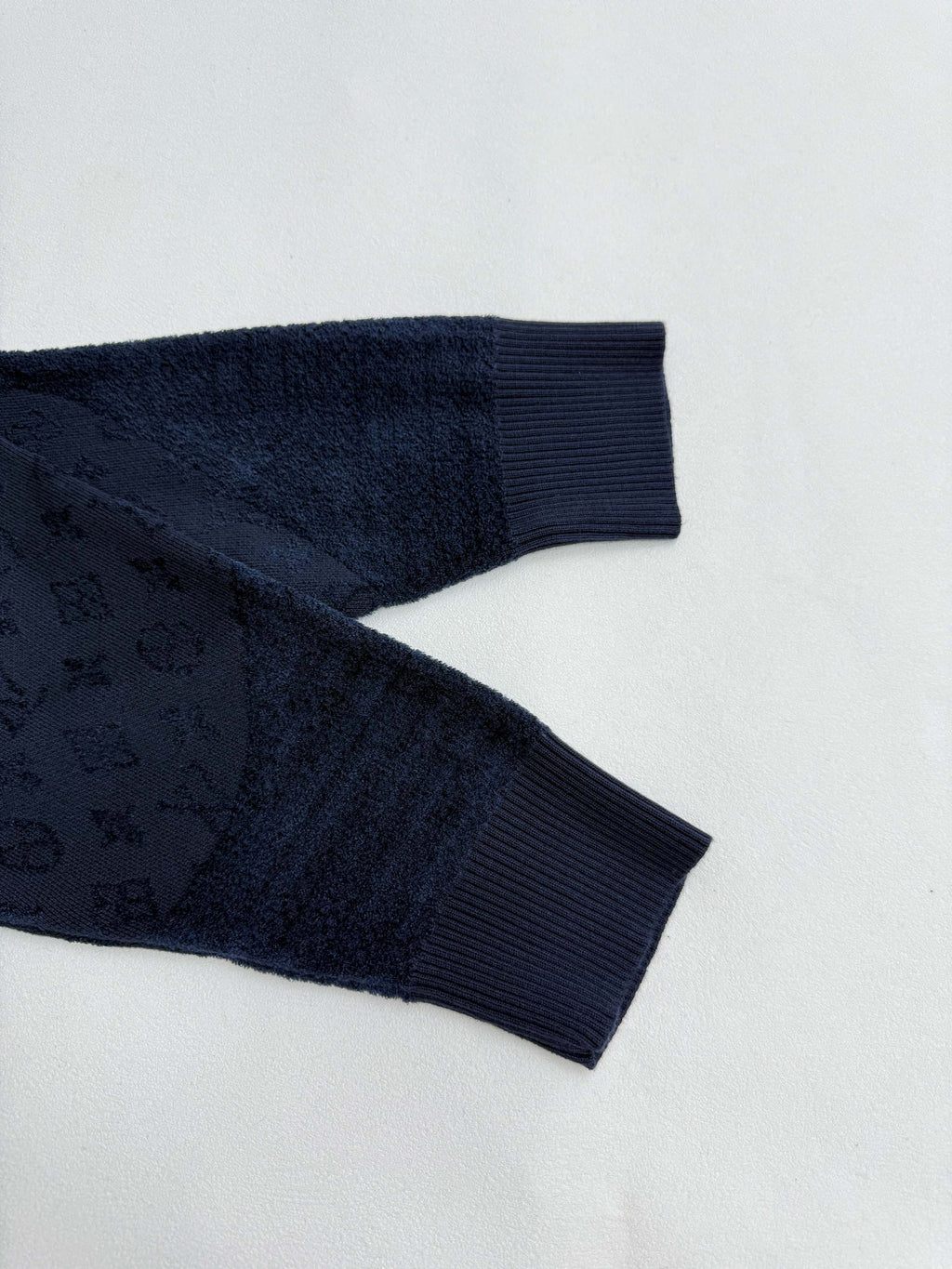 Dark blue ribbed sleeve cuffs and hem with monogram texture, close-up.