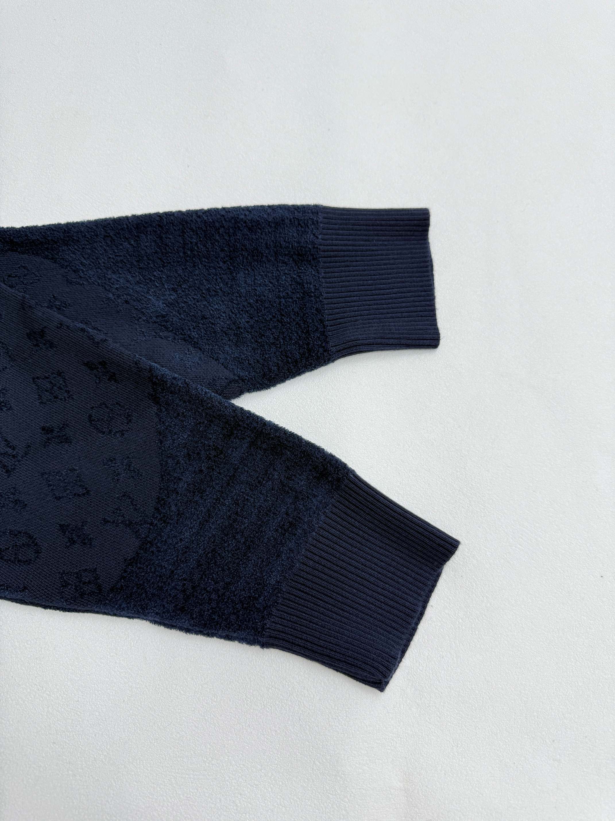 Dark blue ribbed sleeve cuffs and hem with monogram texture, close-up.