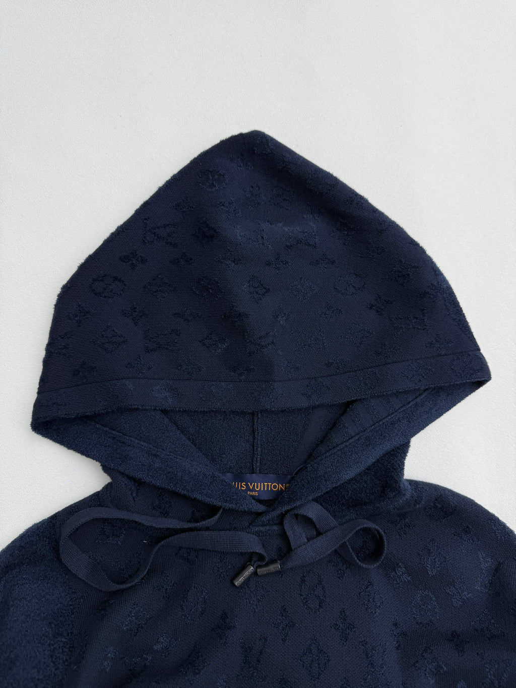 Dark blue monogram hoodie with attached hood and drawstring, close-up.