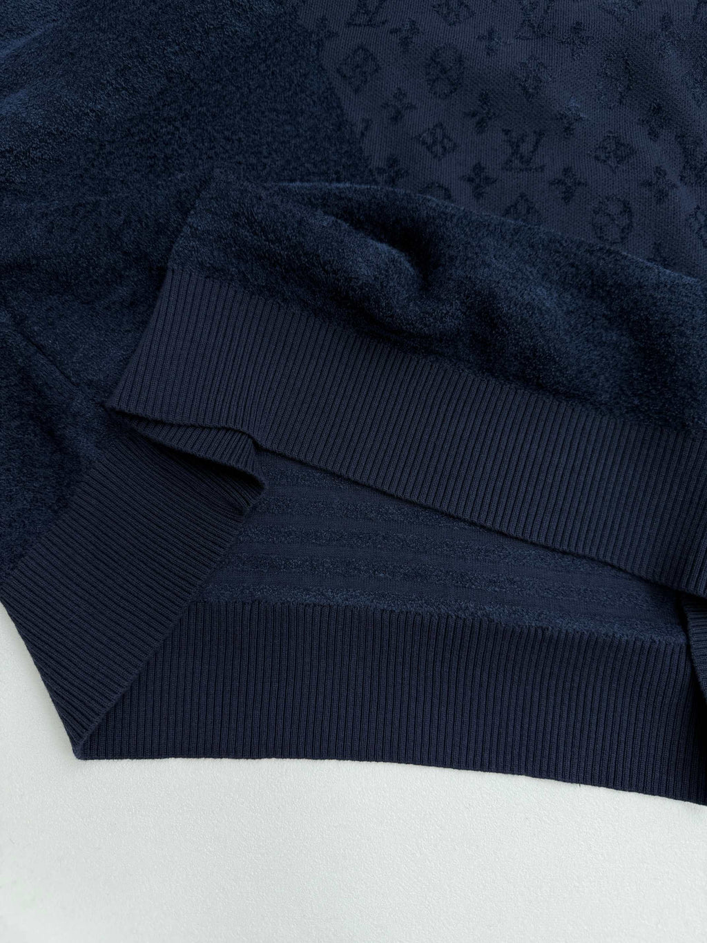 Dark blue hoodie hem with ribbed band and monogram texture, close-up.
