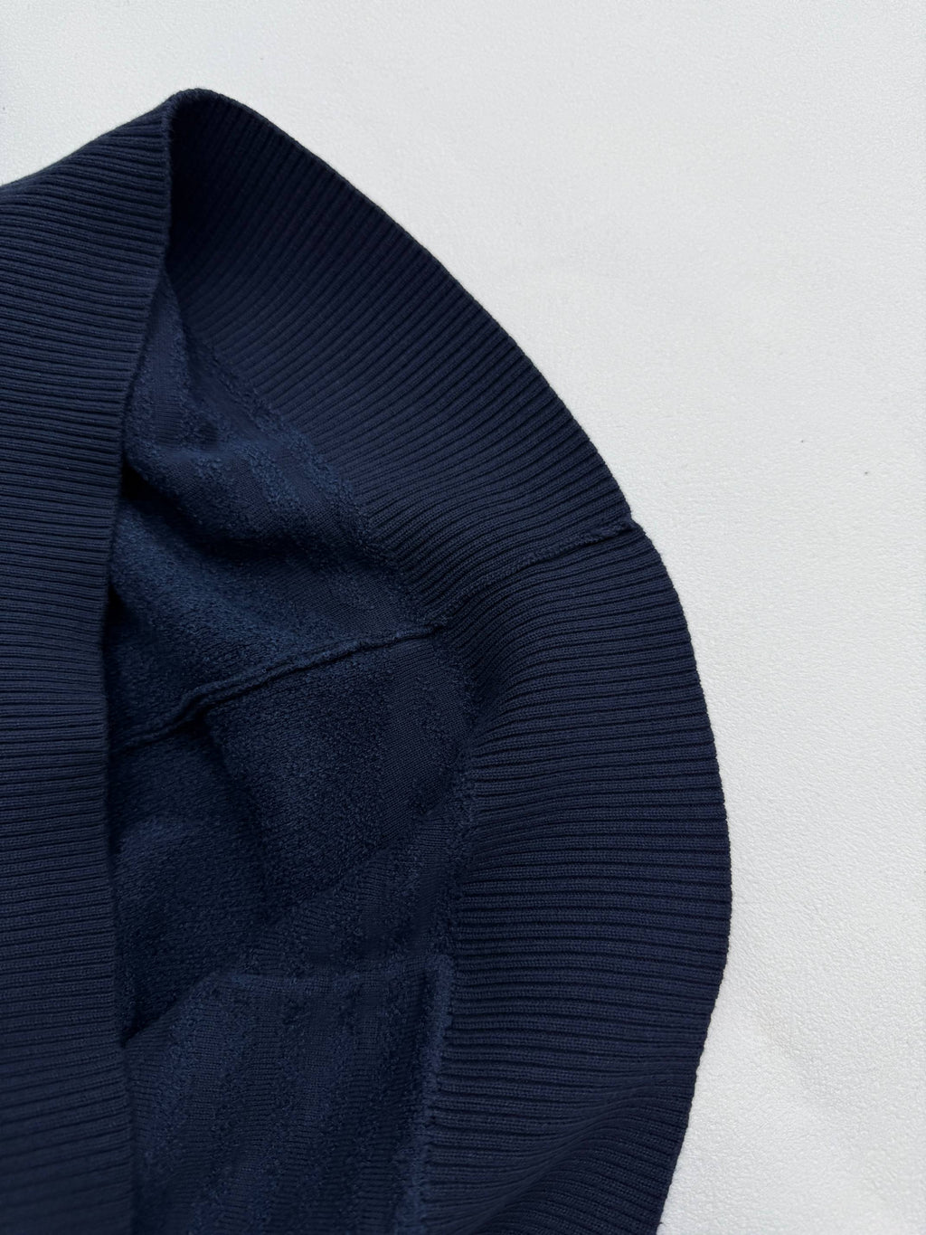 Dark blue hood edge with ribbed trim and monogram texture, close-up.