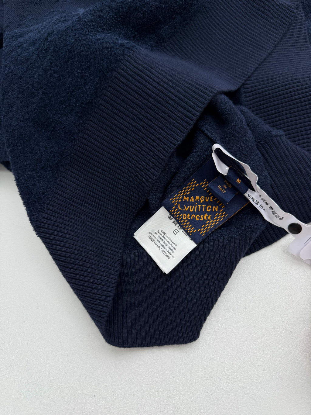 Dark blue hoodie collar with Louis Vuitton swing tag, ribbed trim, close-up.