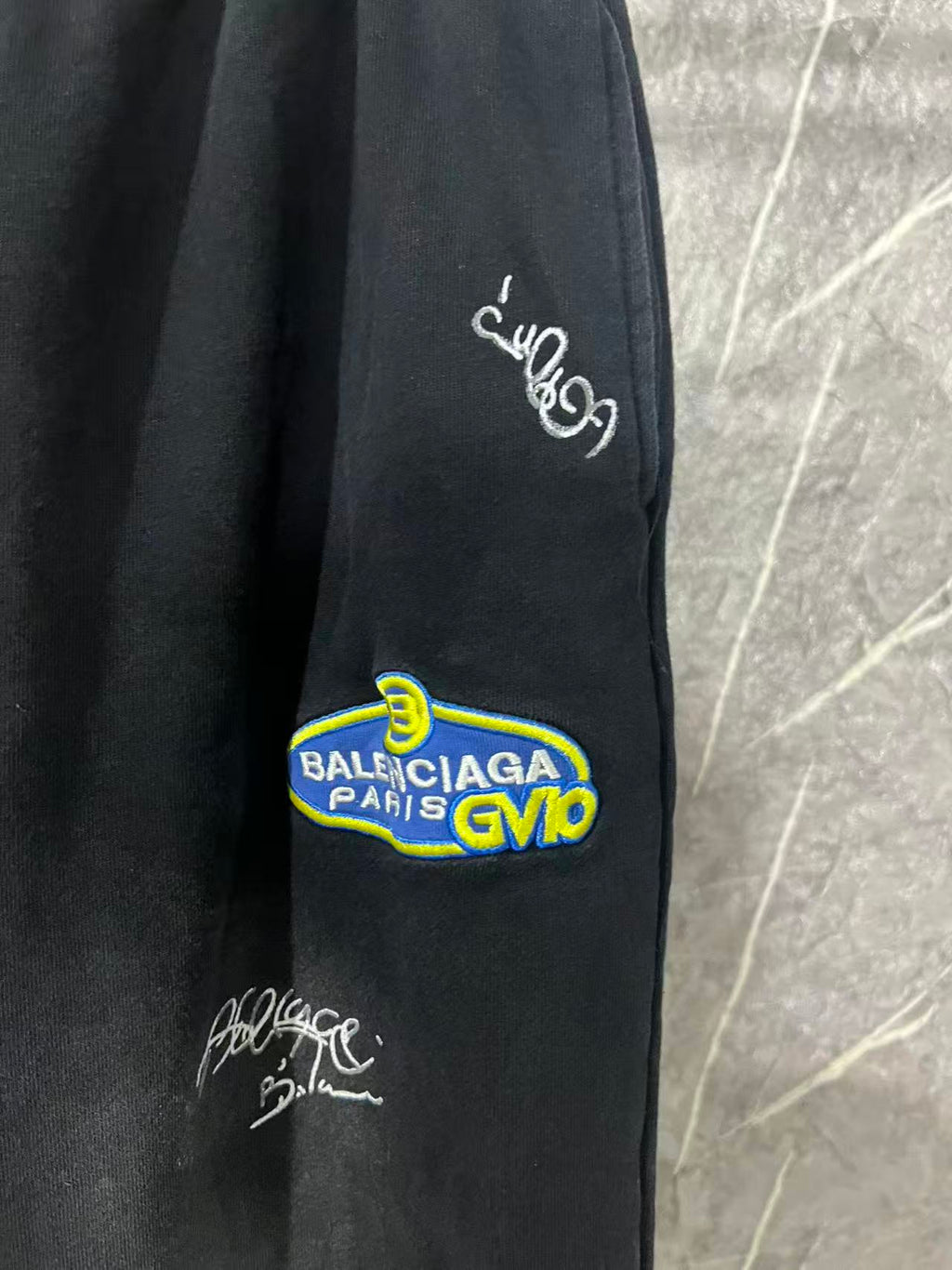 Black pants leg with white script embroidery and colorful Balenciaga-style patch