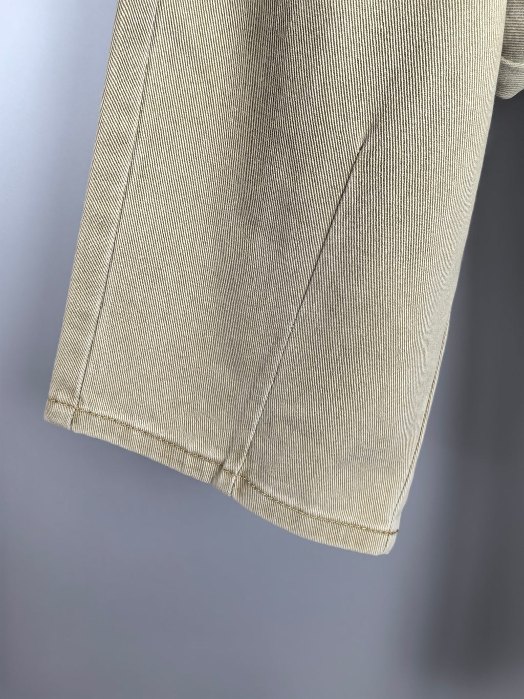 Beige denim pants leg with visible side seam and hem stitching