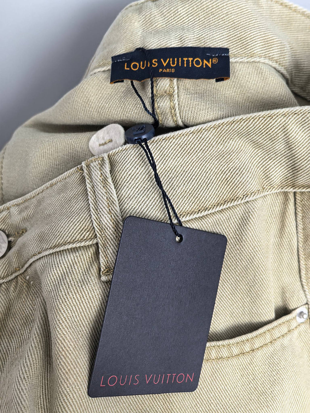Beige denim jacket-style neckline label with attached Louis Vuitton tag
