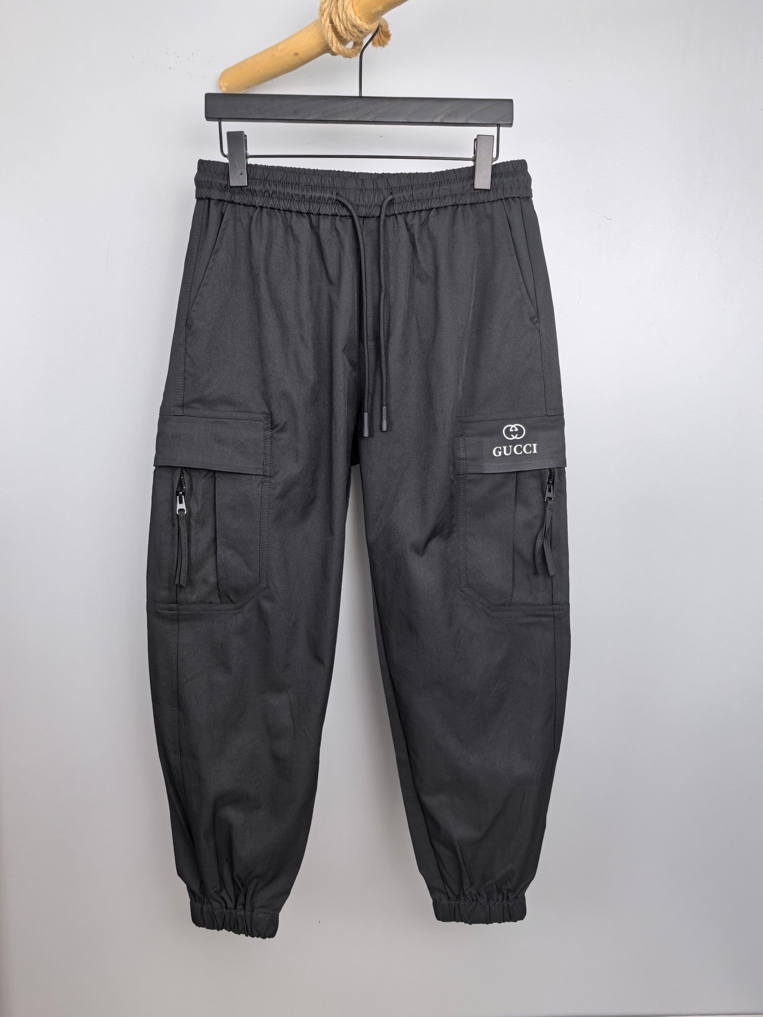 Dark drawstring cargo pants with elastic waist, cuffed legs, side pockets, and GUCCI logo.