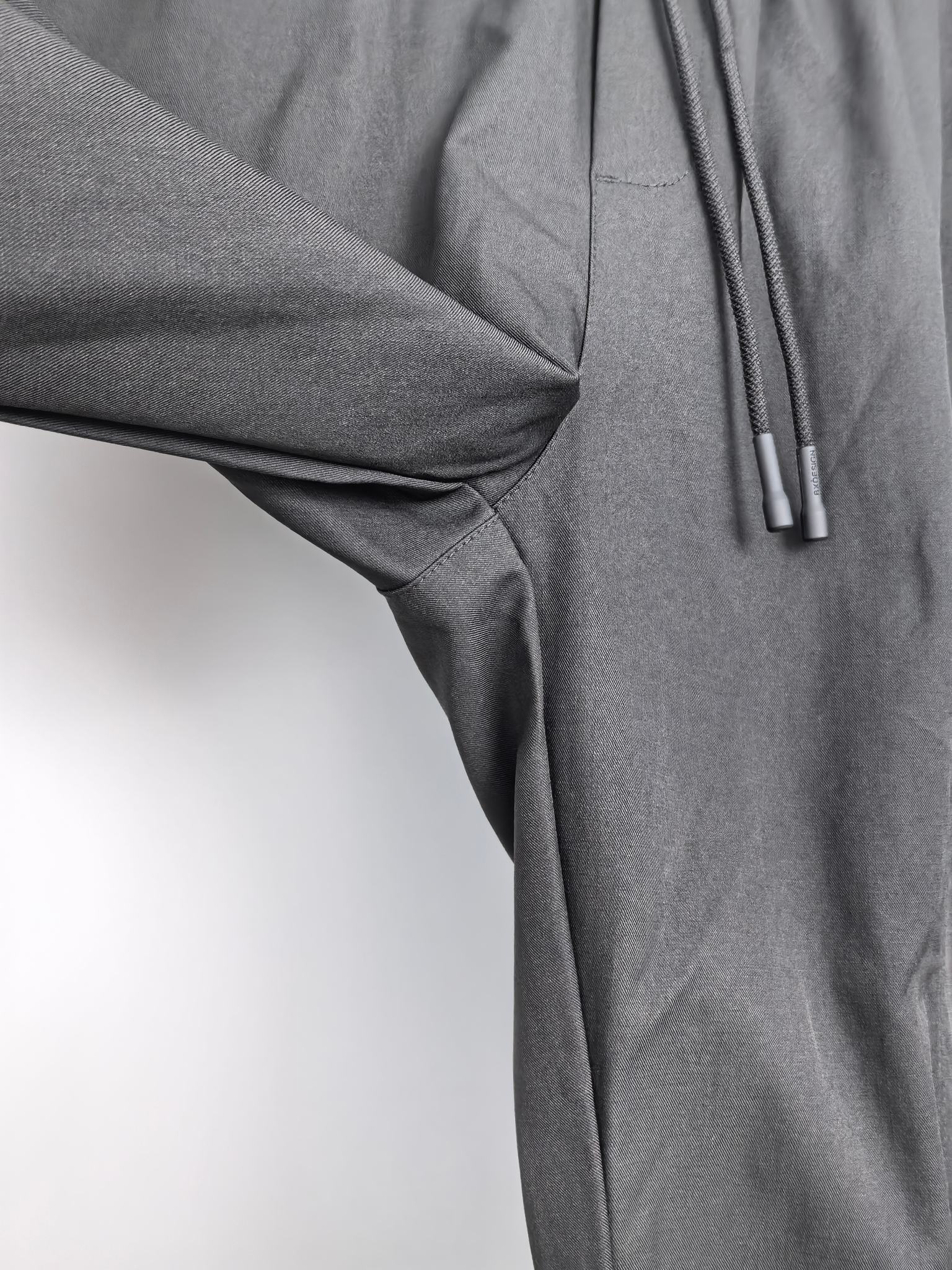 Dark fabric cargo pants detail with drape at knee and drawstring cords.