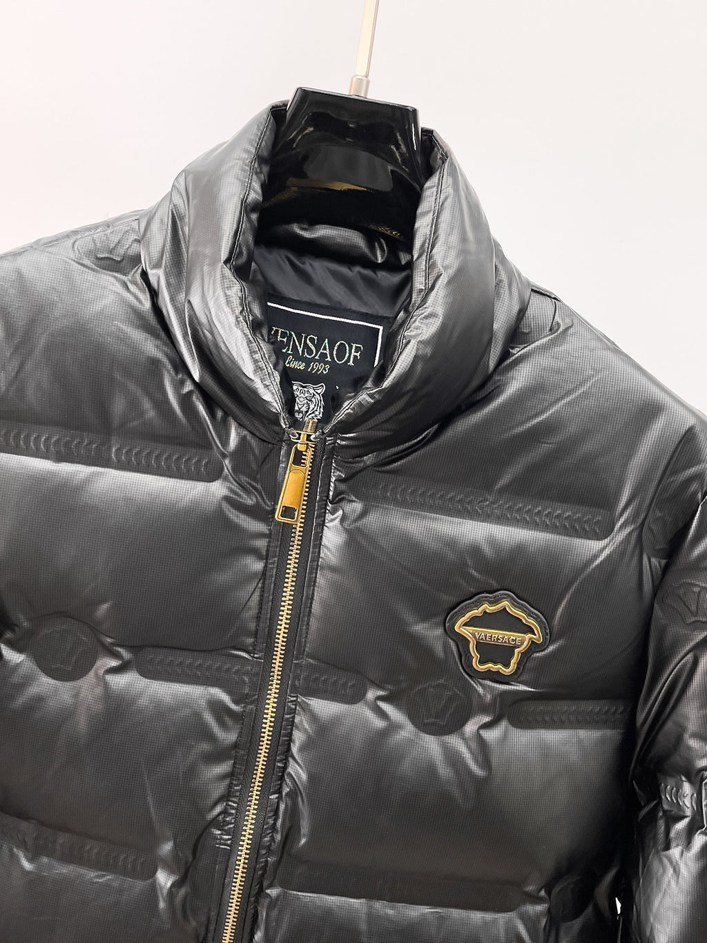 Black puffer jacket close-up of gold zipper, stand collar, and chest patch