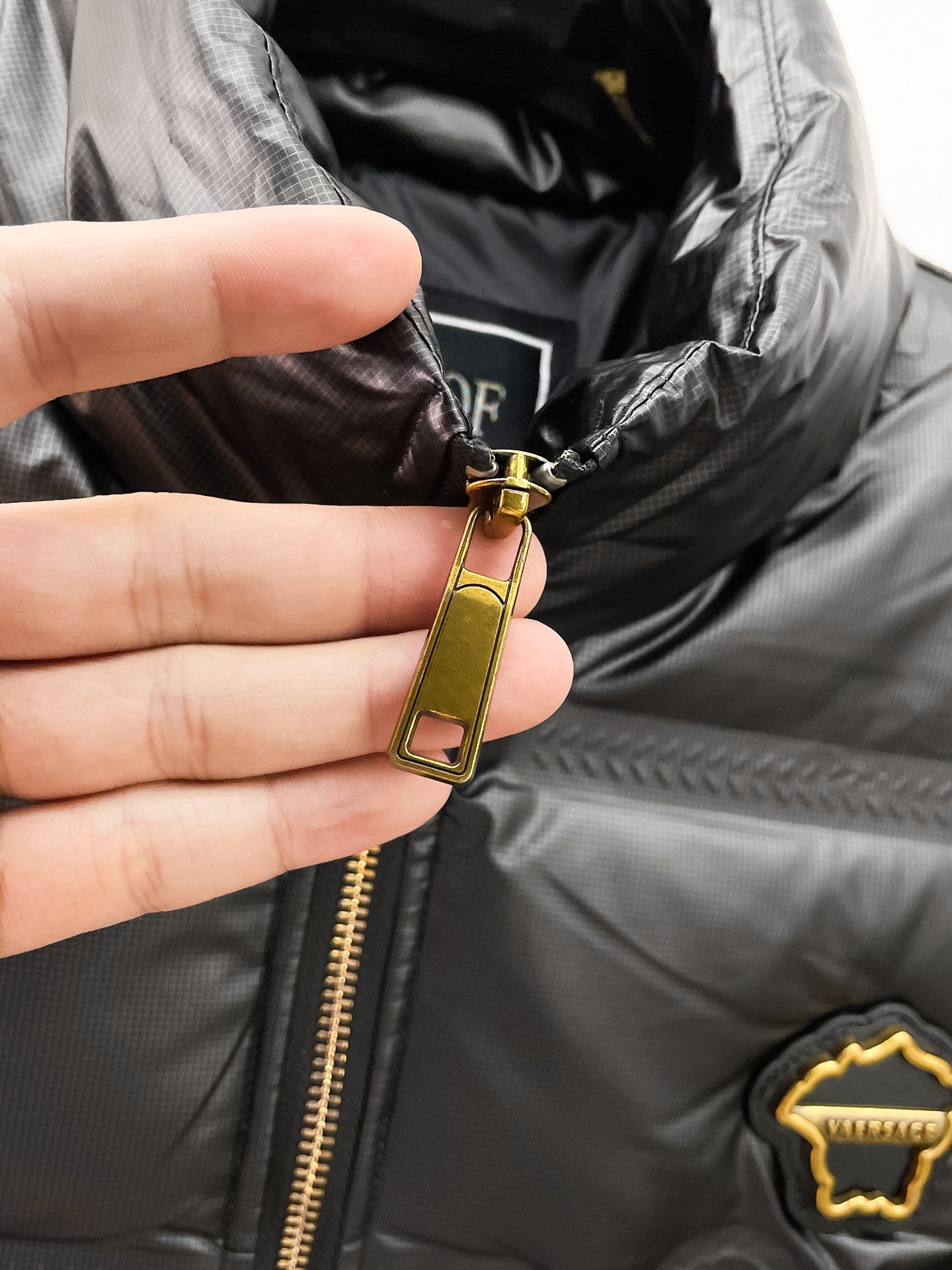 Black puffer jacket close-up of gold zipper pull and inner collar label